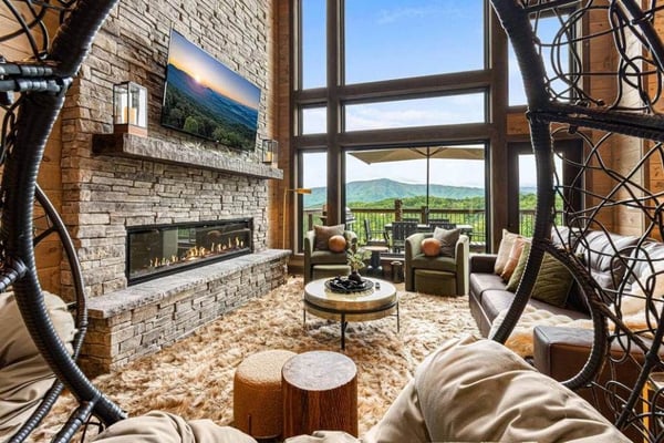Modern living room with stone fireplace, hanging chairs, and mountain views through large windows