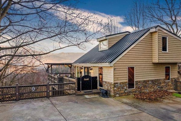 Modern cottage with metal roof and stone foundation on hillside, bare trees and mountain views visible